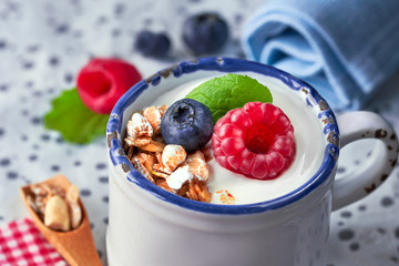Yogurt with muesli, raspberry and nuts, healthy dessert on light spotty background