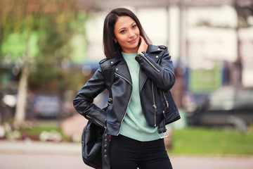 Young fashion woman in black leather jacket walking in city street
