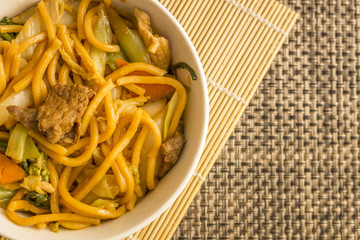 Fried noodle.  Yakisoba with beef, ticken and vegetables in a white bowl on a dark background. Asian cuisine meal.