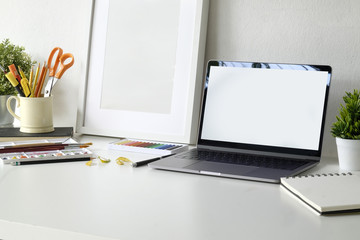 Creative workspace with blank screen laptop and artist craft tools on desk.