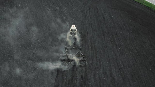 The tractor loosens the ground. The dust is flying. Aerial shot. 4K.