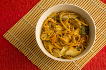 Fried noodle.  Yakisoba with beef, ticken and vegetables in a white bowl on a red background. Asian cuisine meal.