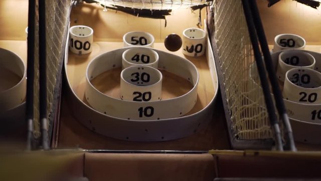 Slo-motion upward shot of a skee-ball bouncing around the baskets of the skee-ball machine.