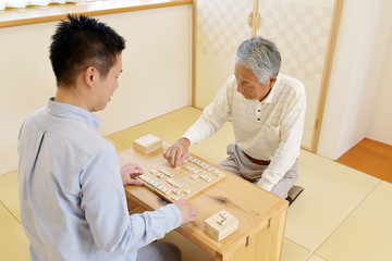 和室で将棋を楽しむシニア男性と若い男性