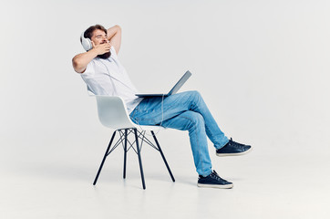 man with headphones laptop sits on a chair on a light background