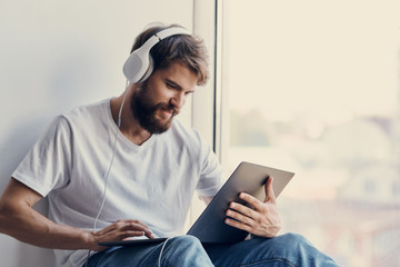 man in headphones sitting by the window with a laptop