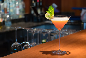A orange color Martini drink on a wooden bar counter.
