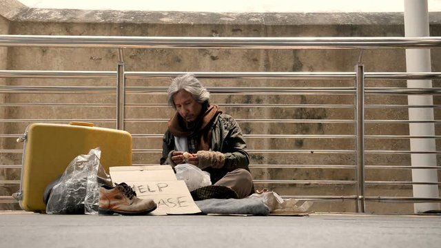 The homeless are scraping fungus from the bread while waiting for donations from person walking on the sidewalk.