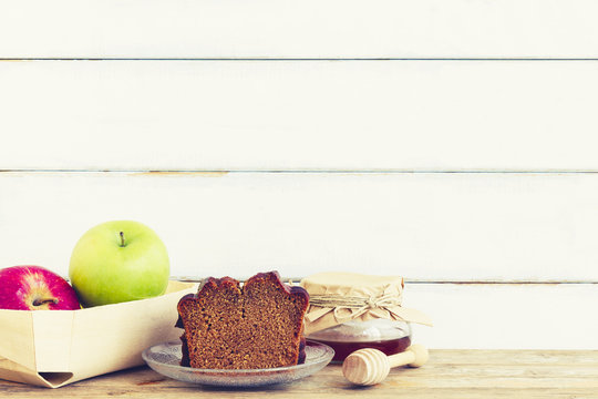 Rosh HaShanah or a Jewish New Year composition including homemade honey cake, apples and a glass jar of honey on vintage or rustic wooden table background