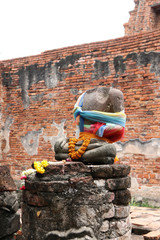 Fototapeta premium There is no head, Incomplete of ancient stone Buddha and worship by colorful fabric and flower in the ruins and ancient remains at Wat Worachet temple, it built in 1593 AD in the Ayutthaya period.