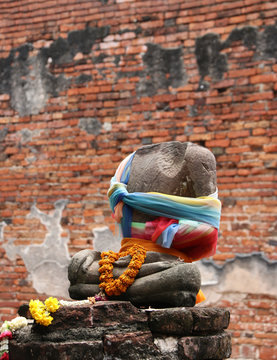 There is no head, Incomplete of ancient stone Buddha and worship by colorful fabric and flower in the ruins and ancient remains at Wat Worachet temple, it built in 1593 AD in the Ayutthaya period.