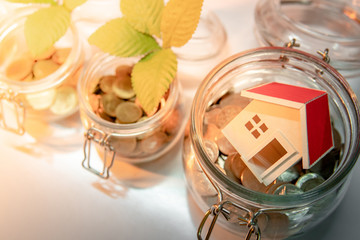 Saving money for retirement concept. Property or real estate investment. Home mortgage loan rate. Coins with green plant and house model in currency glass jars on the table. Business growth background