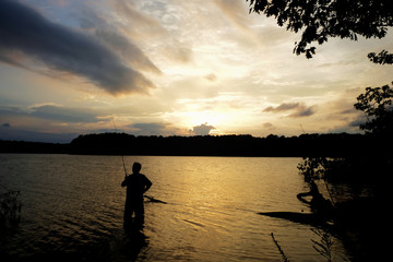 Silhouette of a fisherman standing knee deep in the water at sunset at Lake Benson Park in Garner North Carolina