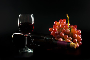 Wine. Bottle and glass of Red wine with ripe grapes still life on black background. .
