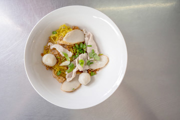A bowl of egg noodle with variety of fish balls and pork in Thai style on stainless steel table.