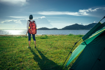 Asian young woman is camping and walking along the road into the forest on weekend, Travel relaxing and adventure concept.