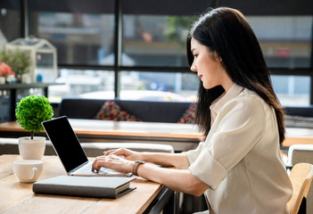 An Asian girl is freelancer woman, she is working by using the laptop computer and drinking a cup of coffee on morning in a coffee shop or her office.