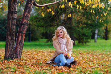 Young beautiful woman sitting on the ground coverd with fallen autumn leaves