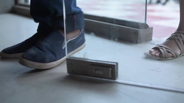 A Boy and a girl enter the glass door of a restaurant, bar or a pub in slow motion, close up of feet and shoes