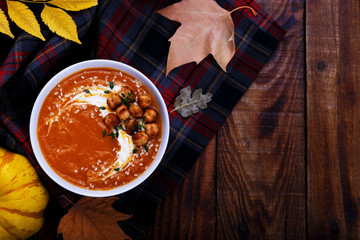 Spicy pumpkin soup with chickpeas on dark wooden table, autumn composition, selective focus