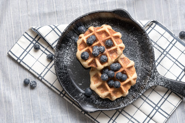 Belgium waffle with blueberry topping in the pan on the tablecloth