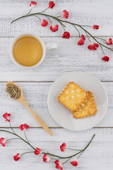 Tea, tea leaves on wooden spoon and biscuit decorate with red paper flowers on white wood background