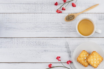 Tea, tea leaves on wooden spoon and biscuit decorate with red paper flowers on white wood background with copy space