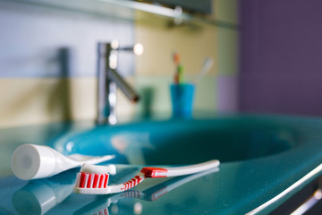 teeth health: brush and toothpaste on blue sink in bathroom. red toothbrush lies in the interior on...