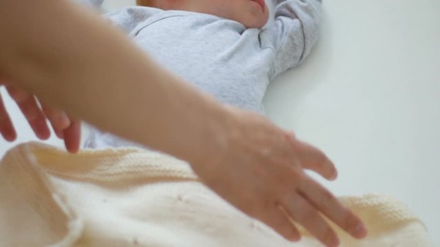 Mother cover her baby with a blanket in a white bed, warm concept and healthcare