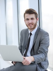 young professional with laptop on background of office window