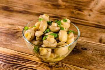 Canned mushrooms in a glass bowl on wooden table