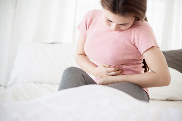 Young asian woman suffering from abdominal pain on the bed.