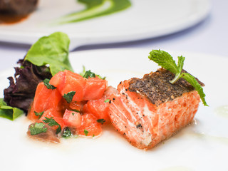 Salmon steak with fresh salmon sashimi served on white plates.