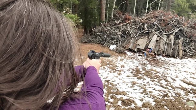 A woman shooting a 22 pistol with a suppressor on it in slow motion.
