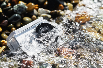 White action camera with underwater case in water on the pebble beach