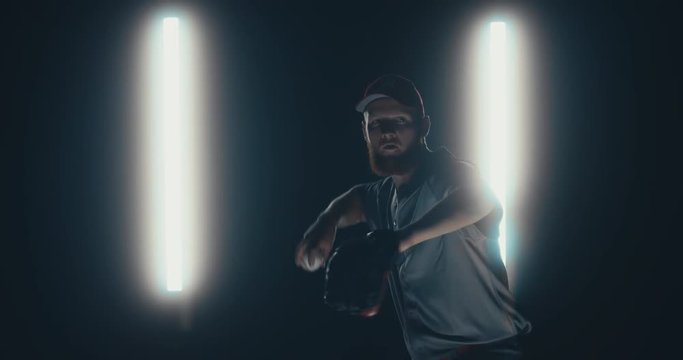 Caucasian professional baseball player pitcher throwing a ball towards camera against dark background. 4K UHD 60 FPS SLOW MOTION