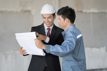 Businessman is wear white helmet stand with engineer. They are looking at blueprint in them hand....