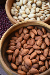 close up of almonds and pistachios in wooden bowl on red bean background