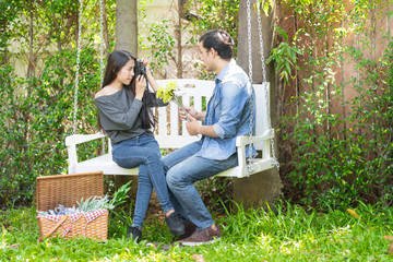 Sweet Love Couple Picnic in the Garden Park on Weekend Having Lunch and Chill out with Beautiful Nature. Girl taking a photo with her boyfriend.