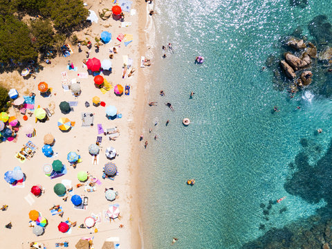 View from above, aerial view of an emerald and transparent Mediterranean sea with a white beach full of beach umbrellas and tourists who relax and swim. Costa Smeralda, Sardinia, Italy.