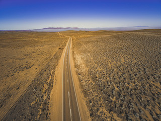 Rural road passing through dry land with scarce vegetation at sunrise  - aerial panorama