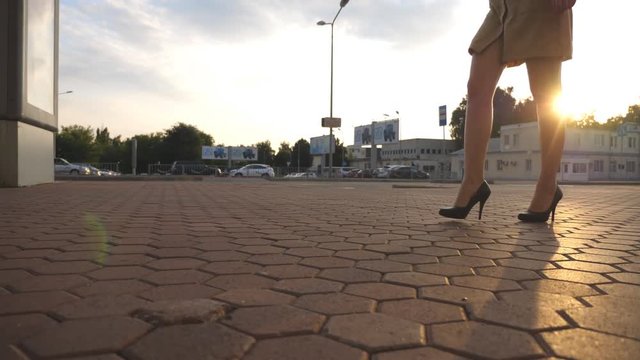 Female legs in high heels shoes walking in the urban street. Feet of young business woman in high-heeled footwear going in city. Girl stepping to work. Sun flare at background. Slow motion Close up