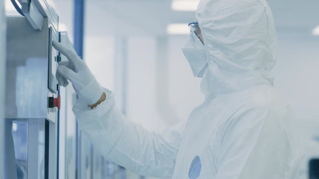 In the Manufacturing Facility Team of Scientist Wearing Sterile Protective Coverall Set's up / Programs Modern Industrial 3D Printer, High Precision Manufacture of Semiconductors under Process.