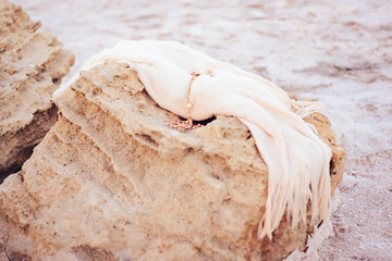 a gold ornament with pink pearls lies on a white cloth unfolded on a stone among a salt lake.
