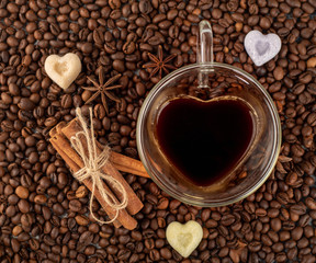 Coffee cup in the shape of heart on coffee beans with sinnamon and anise background. Top view.