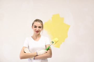 Female decorator painting wall with roller indoors