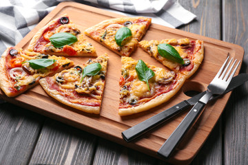 Board with tasty sliced pizza on wooden table