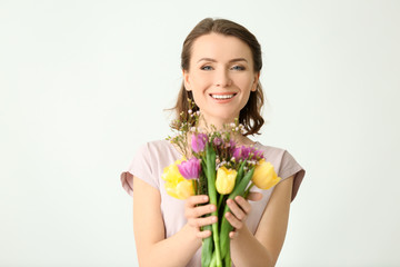 Beautiful woman with bouquet of flowers on light background