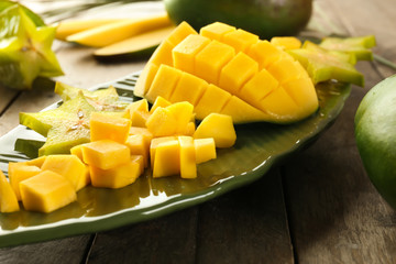 Plate with pieces of fresh mango and starfruit on wooden table, closeup