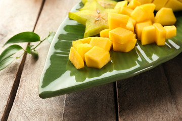 Plate with pieces of fresh mango and starfruit on wooden table, closeup